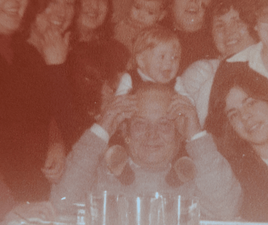 En esta foto antigua aparezco yo cuando era bebé subida sobre los hombros de mi abuelo rodeados de toda mi familia. Parece una celebración familiar.